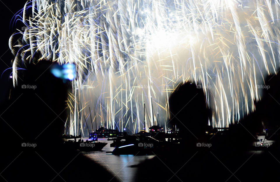 Image showing a human silhouette taking cell phone images in front of a huge firework called Seenachtsfest in Konstanz. Golden and blue sparkles reflecting on lake constance