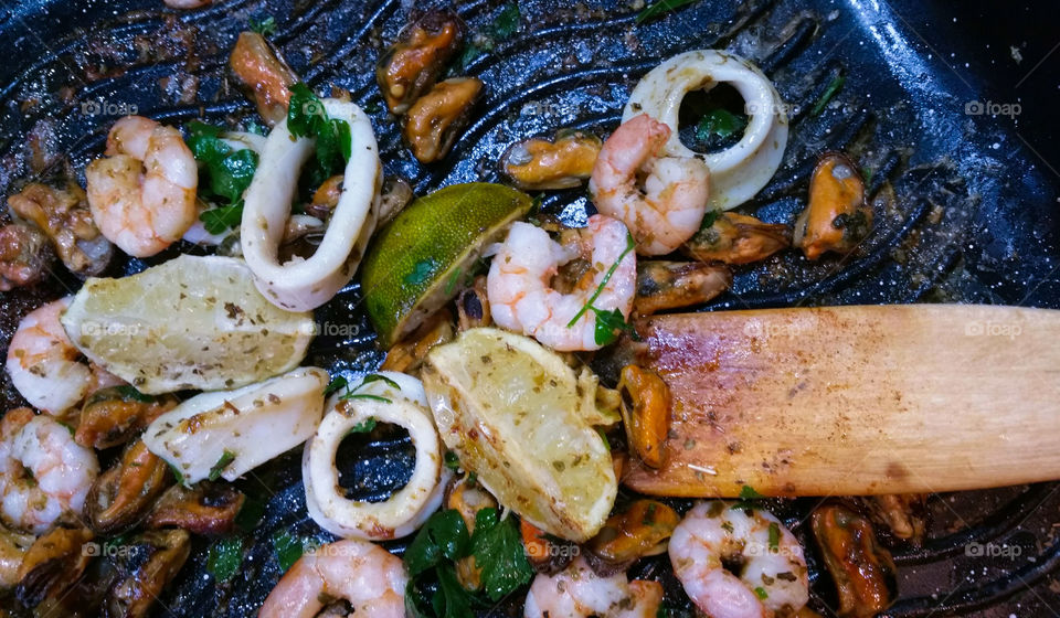 Frying calamari fish with lime wedges and parsley