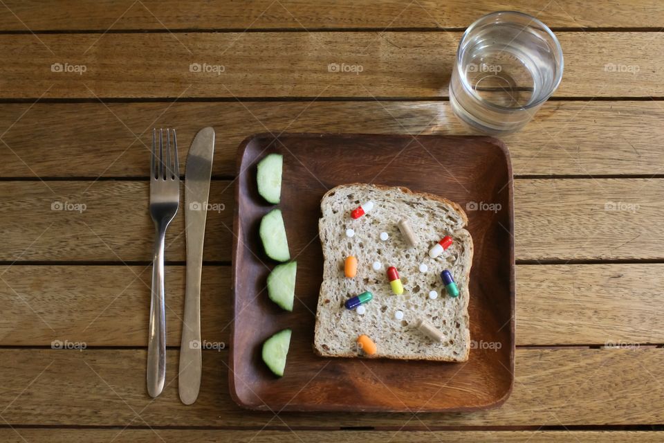 A variety of pills on a slice of bread on a wooden plate with a glass of water