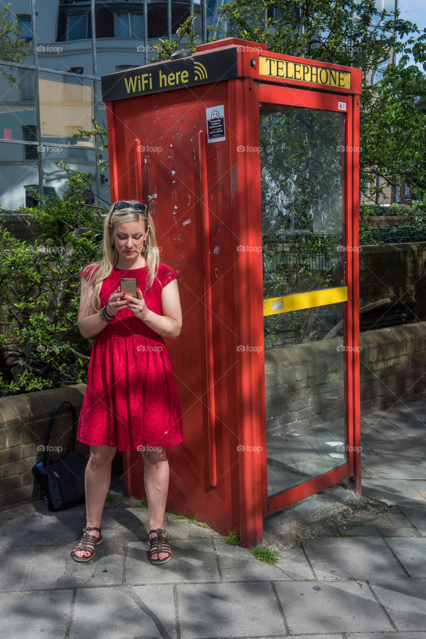 Woman 30 years old looking at her phone and social media at at WiFi spot at a telephone booth in London near Euston Square.