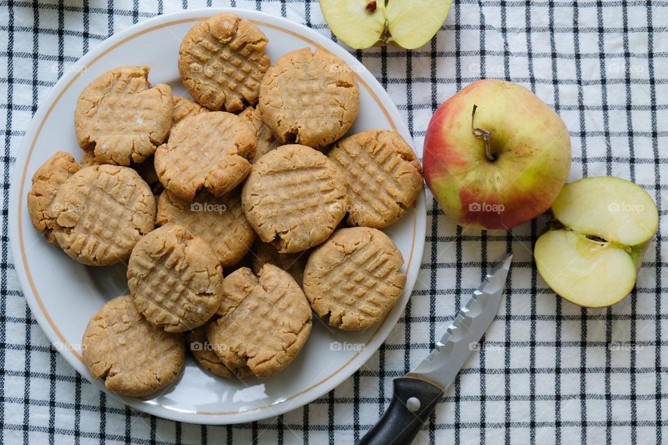 Flat lay with American peanut butter cookies, cut apple, dried flowers and khife on the checkered napkin