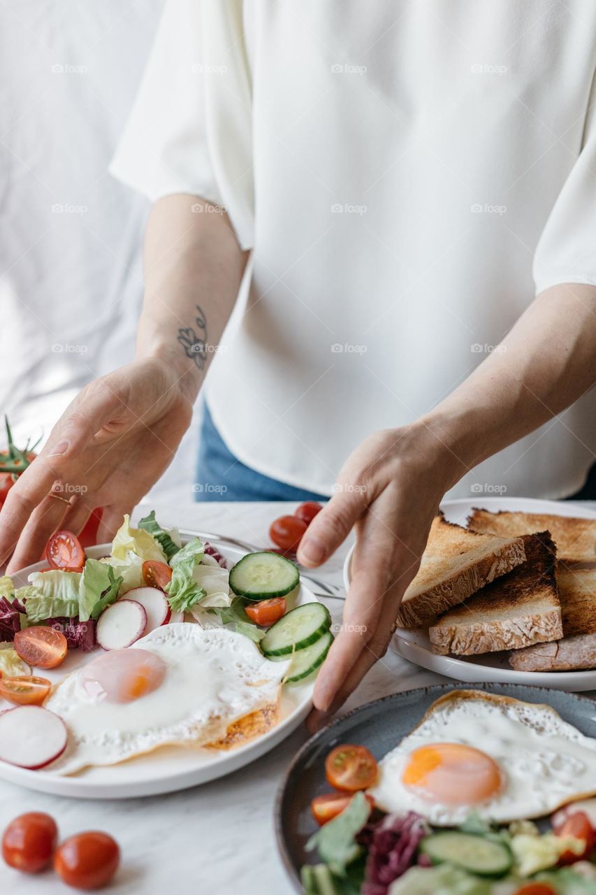 Woman serving a healthy brekfast, with eggs, vegetables and bread.