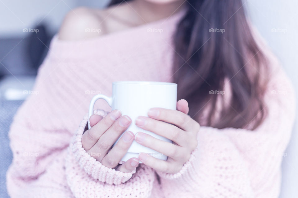 A woman wearing a cozy sweater and holding a cup