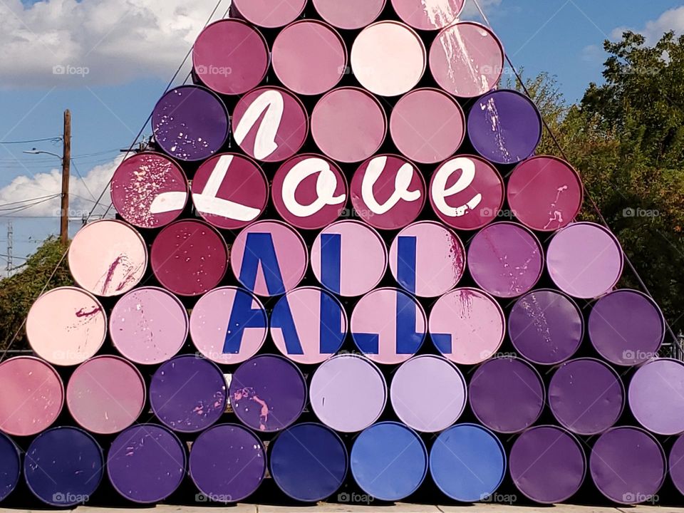 Street art with a message -colorful painted steel drums stacked in a triangle shape with the words Love ALL.