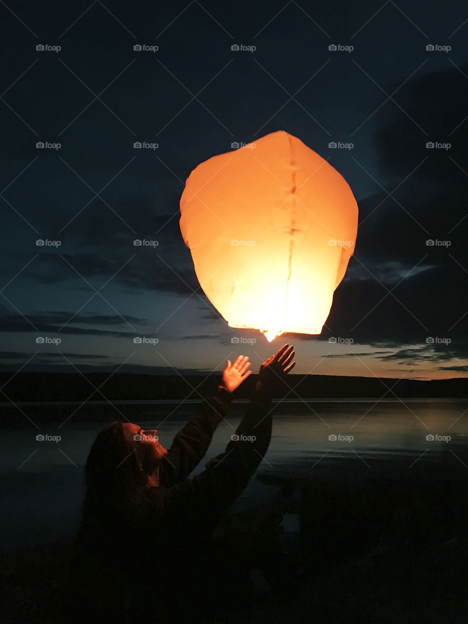 Young woman running Chinese lantern into the sky in the evening above the lake 
