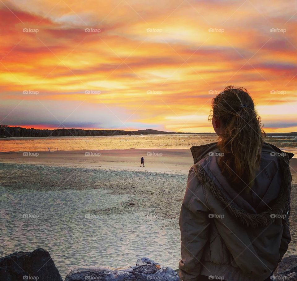 Girl with pony tail looking at the red orange sunset at the beach 