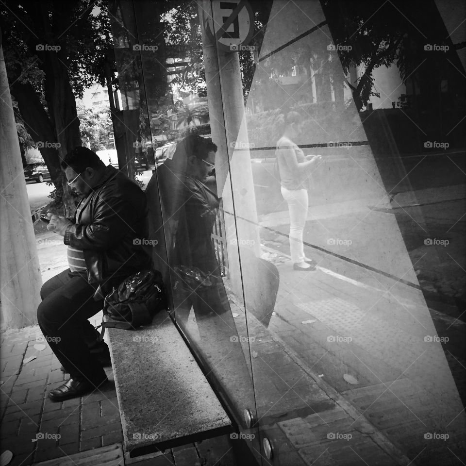 Men looking at his mobile phone at a city bus stop