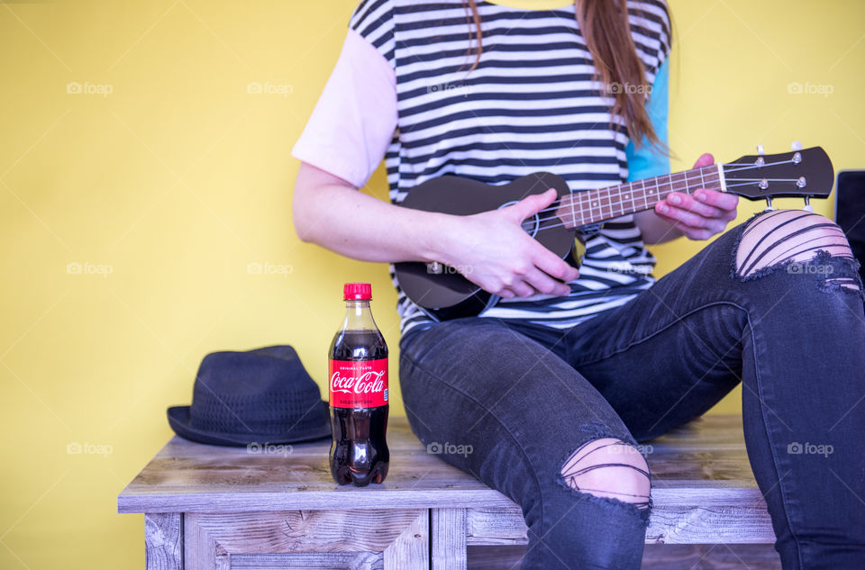 Young woman sitting next to a bottle of Coca-cola while playing a ukulele