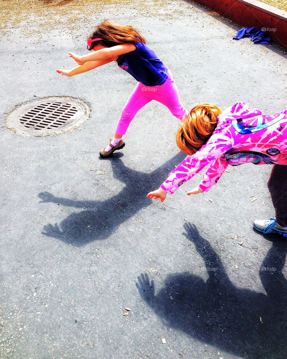 Two young girls in bright pink clothes doing cartwheels at recess in