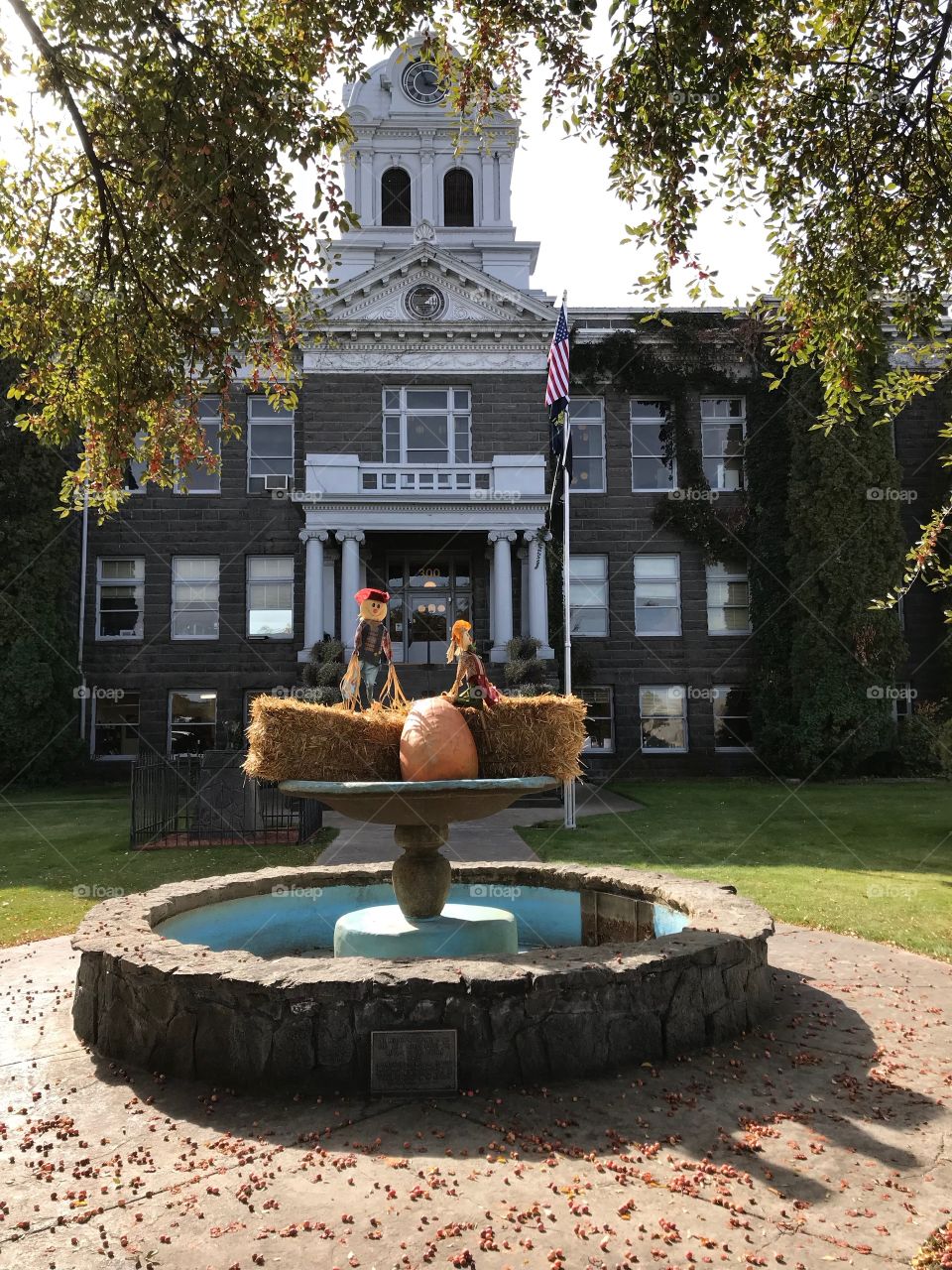 A pair of decorative scarecrows perched on hay bales with a pumpkin in the fountain at the old Crook County Courthouse in Prineville in Central Oregon on a beautiful fall day. 