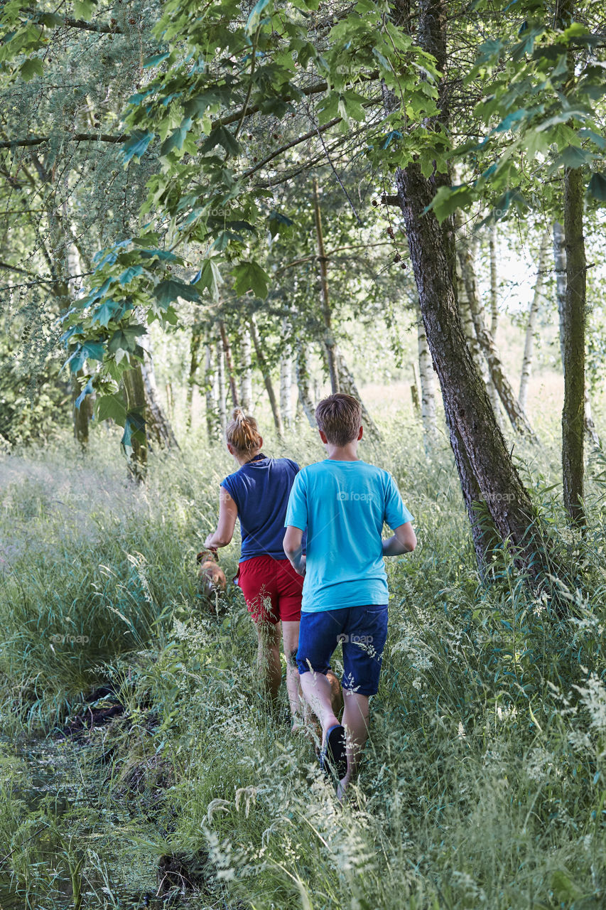 Mother and her son walking along a path, among the trees, close to nature, during summer vacations. Candid people, real moments, authentic situations