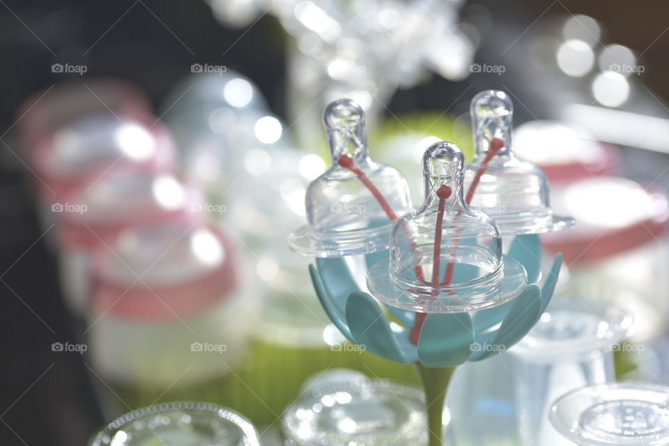 Drying baby bottle nipples in the foreground and baby bottles blurred in the background.