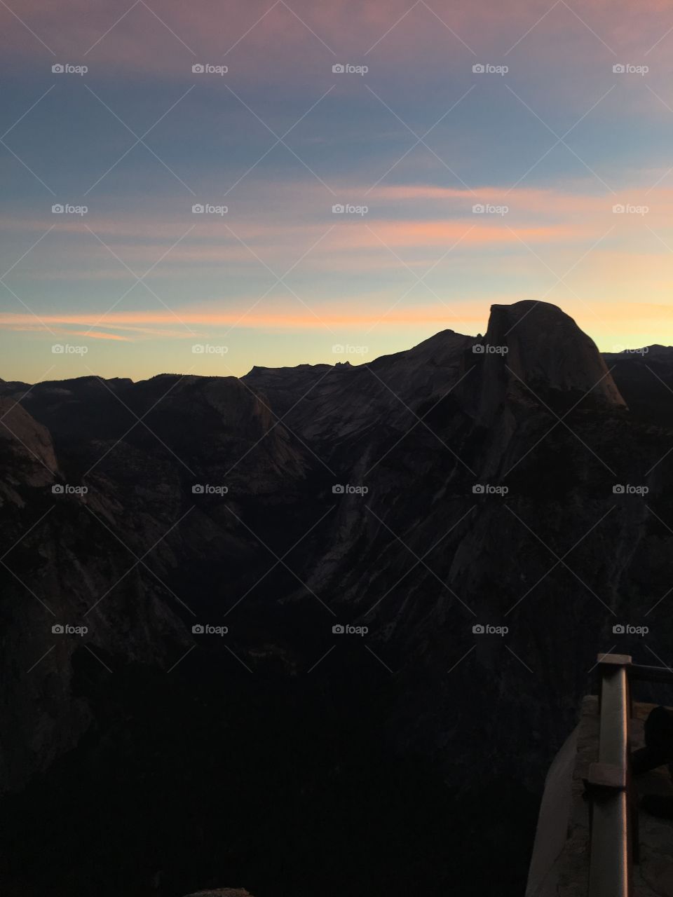 A view of Half Dome Mountain in Yosemite at dawn I. The fall on a clear day with slight wispy clouds allowing the sunrise to light up the sky with tones of orange and pink contrasting the deep and light blues of sky as the sun rises. 