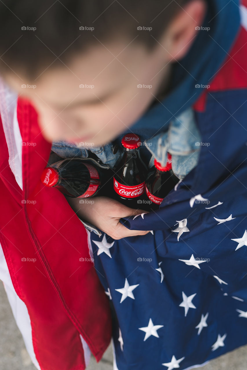 the guy sits on a bench, on his shoulders the flag of America, in the hands of Coca-Cola.  Street, spring