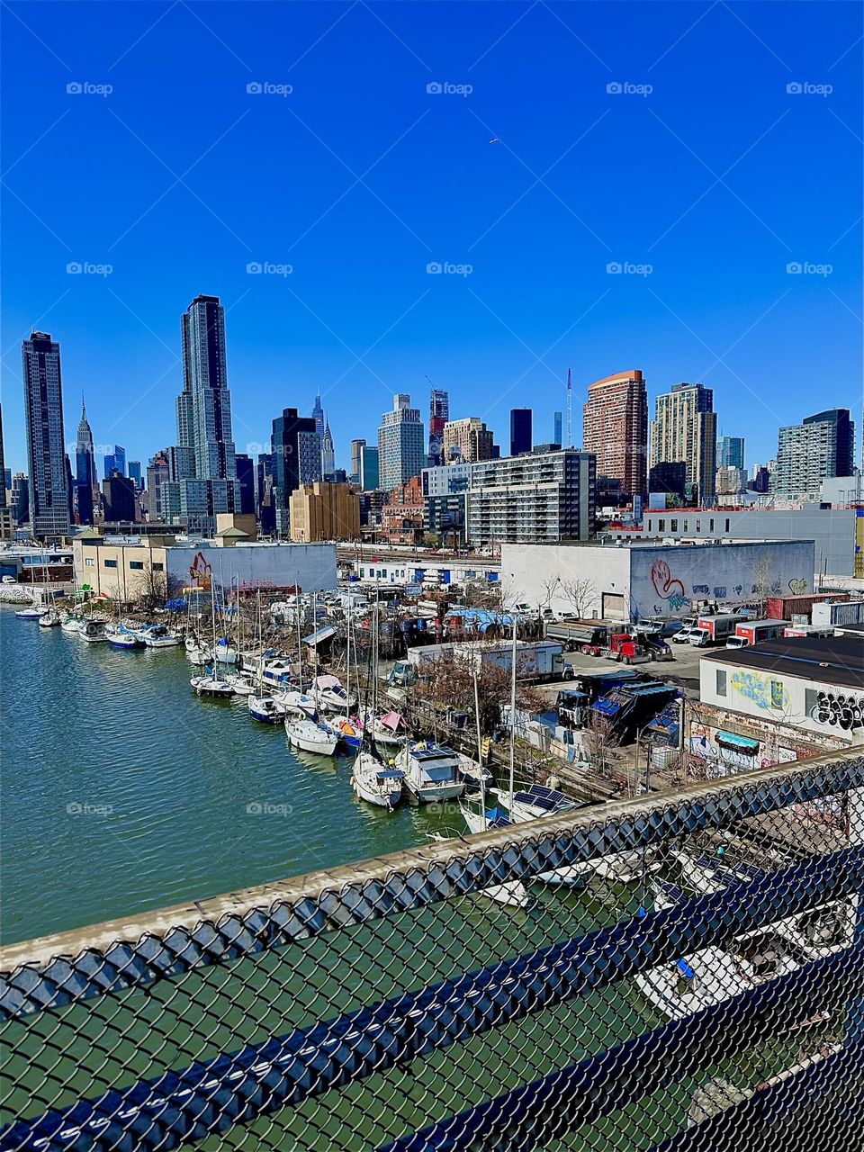 This is “Newtown Creek” with its many boats seen from the “Pulaski Bridge” that connects LIC, Queens to “Greenpoint”, Brooklyn. In the far distance we can see “Manhattan”. 2024. Hypnotic Productions