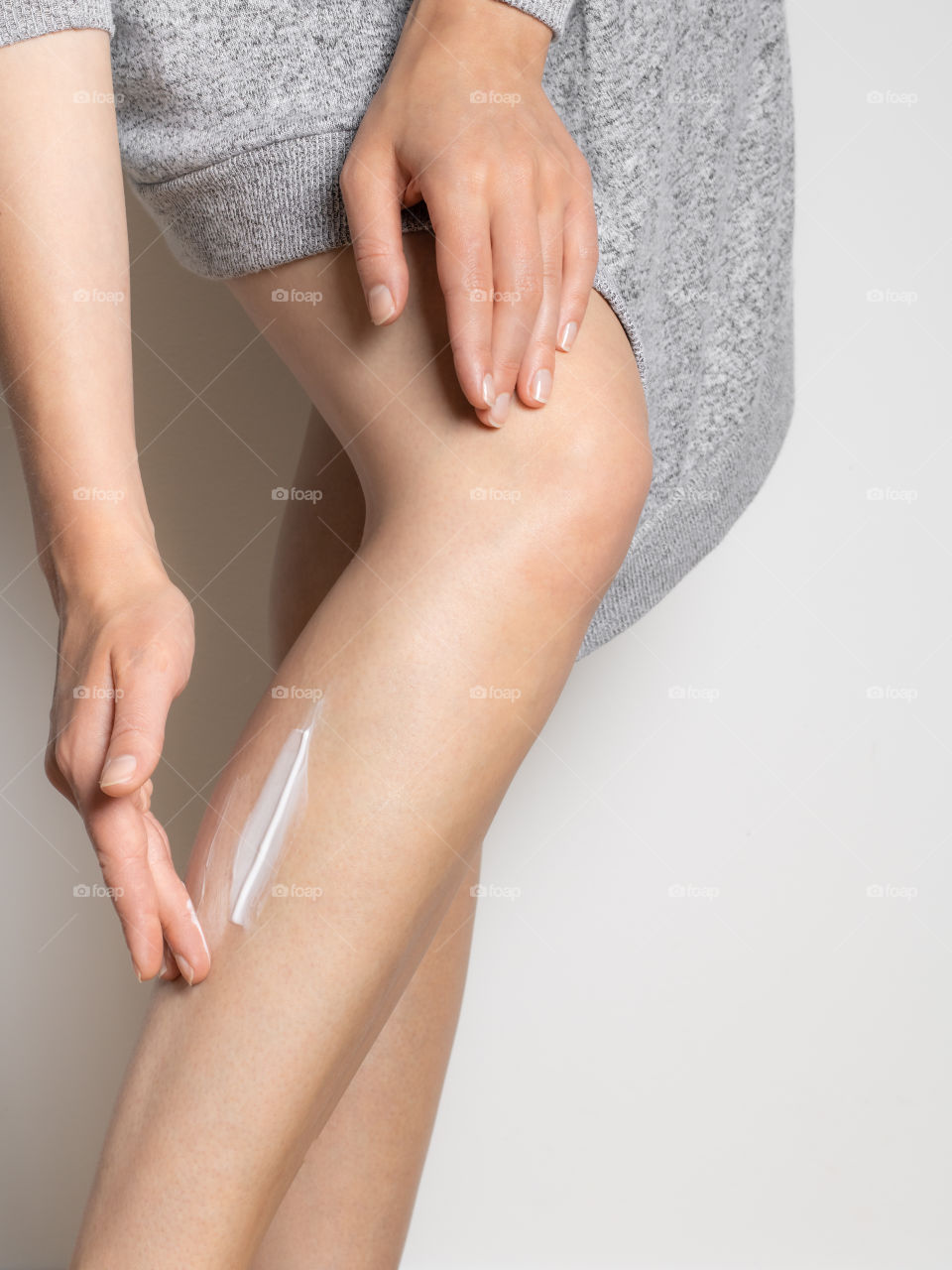 Young woman using body lotion, leg cream