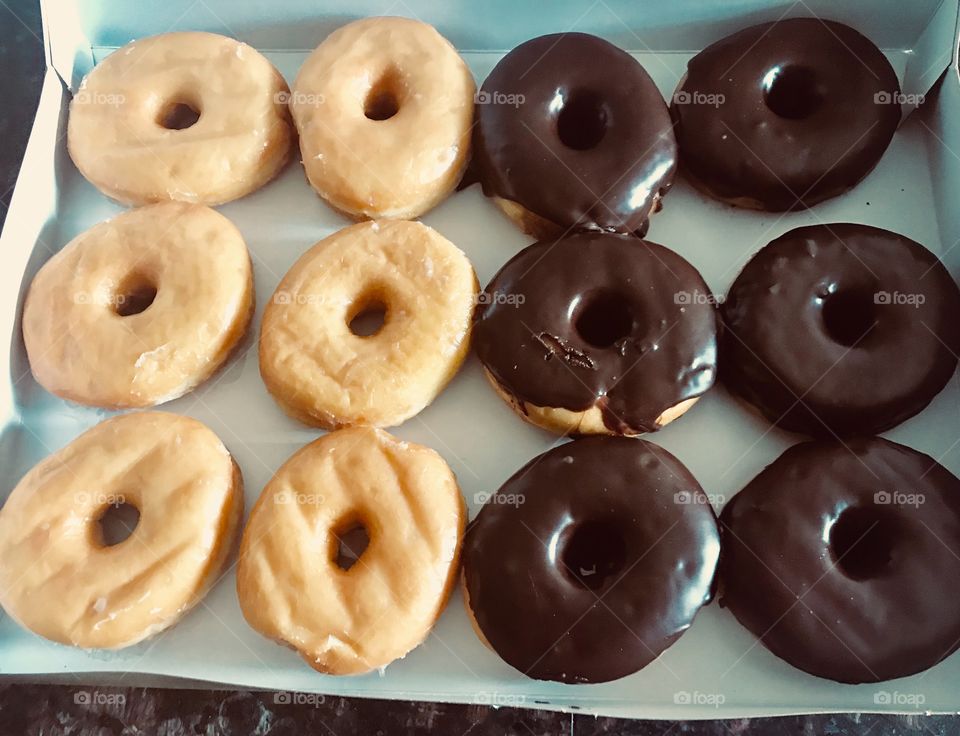 Delicious: glazed and sugary chocolate covered donuts displayed any donut box on the kitchen counter ready to be eaten.