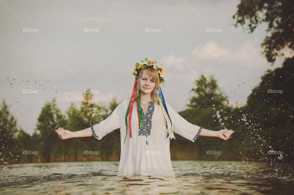 Happy Ukrainian girl,  woman in embroidery, wreath of flowers swimming in green lake in summer. Support Ukraine. Symbol