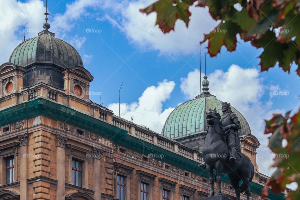 close-up of the Grunwald Monument with King Władysław Jagiełło on top. In the background, a beautiful tenement house on Jan Matejko Square