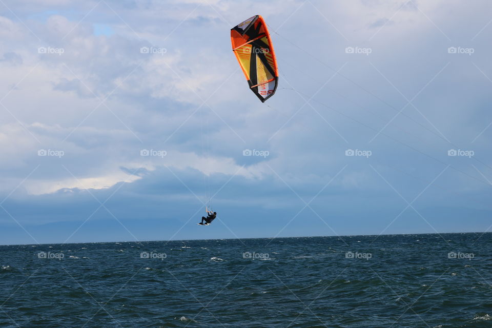 Kitesurfer jumping in the air against cloudy sky