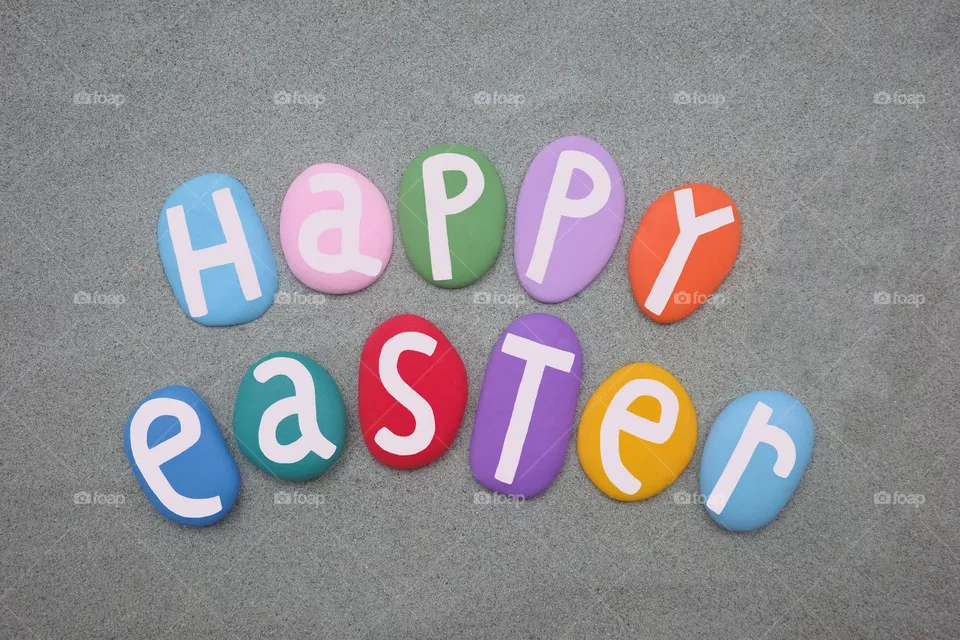 Happy Easter message composed with hand painted stone letters over green sand 