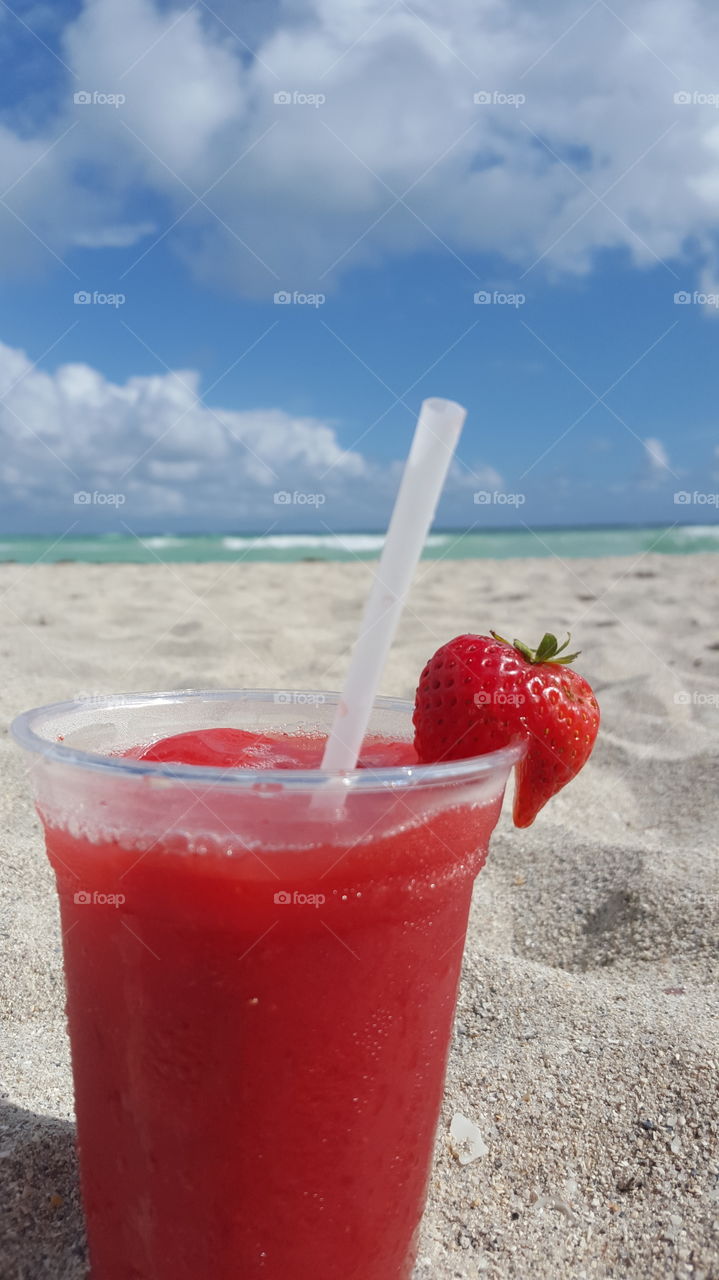 Glass of strawberry juice on beach