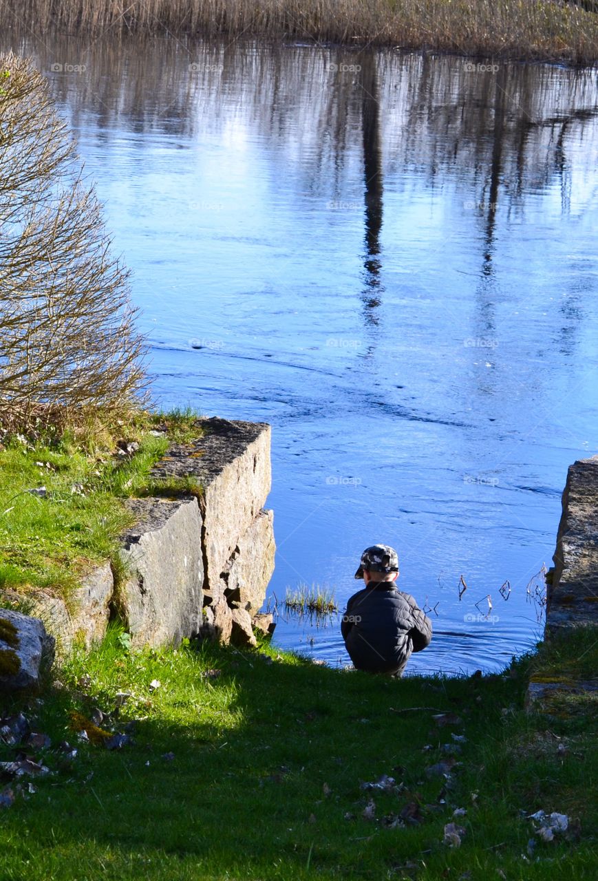 Boy sitting at the river. Boy playing with the water