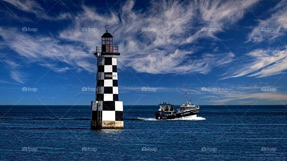 The Perdrix lighthouse and a fishing boat passing by under a bright blue sky filled with white clouds in Tudy island