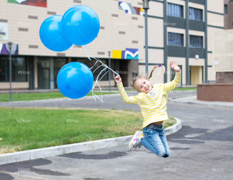 Happy girl jumping in mid-air with blue balloons