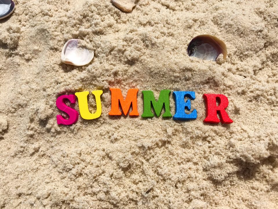 Wooden letters on sandy soil, the word summer