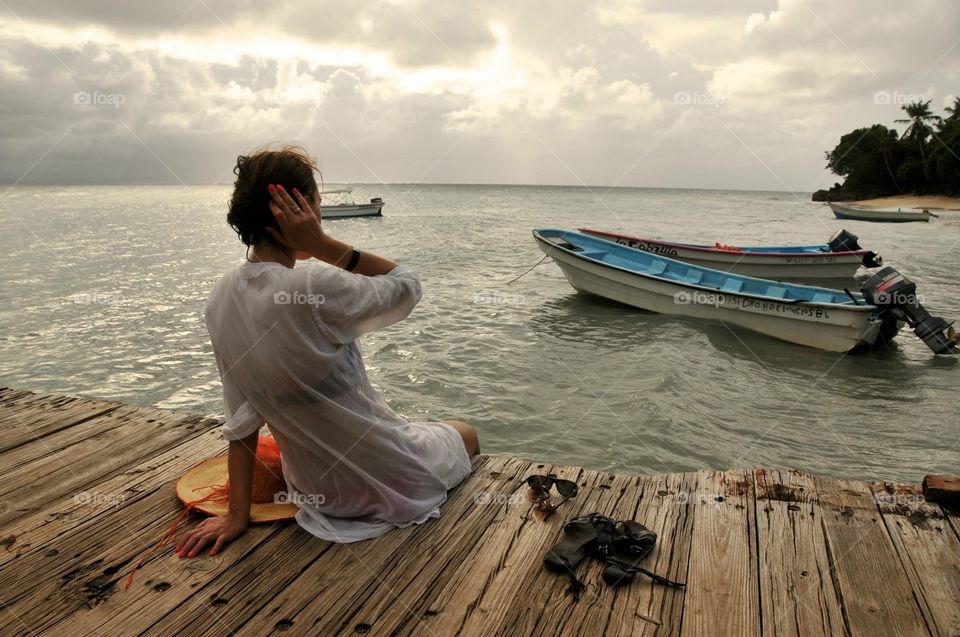 Woman is taking rest on the wooden bridge and observing ocean