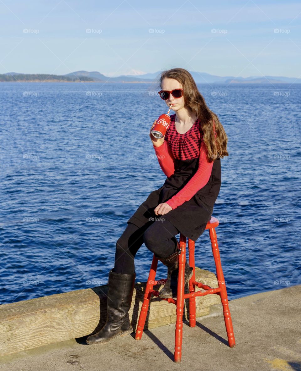 Girl in red stool drinking cola on an scenic ocean pier