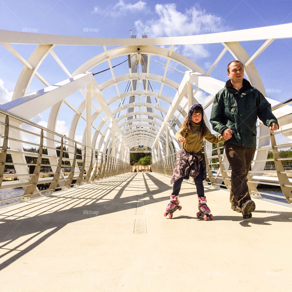 Daughter skating on bridge with her father