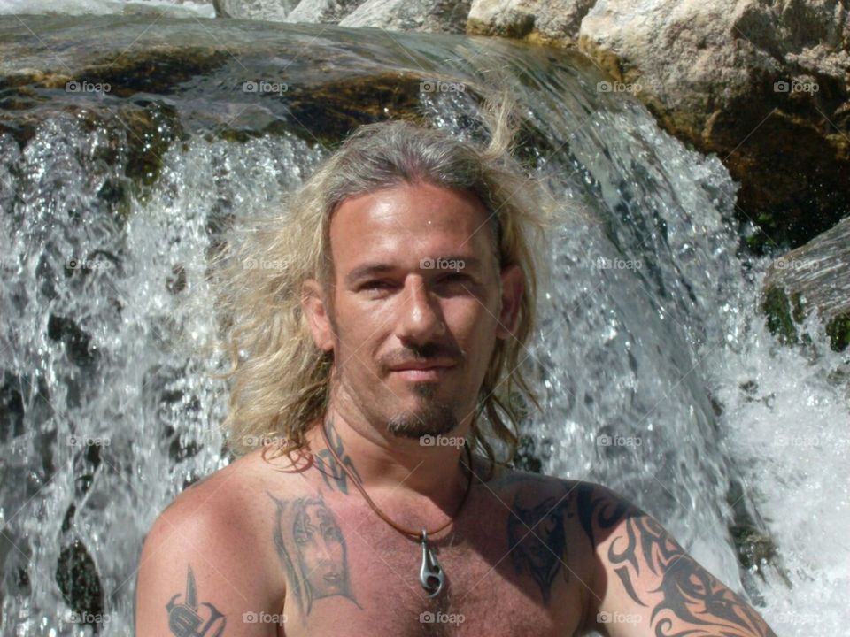 Man with hair in the wind posing in front of the waterfall.