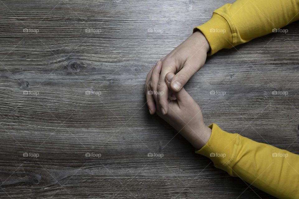 Men's hands in a yellow jacket lie on a gray wooden surface, which is used as a background or a surface with incident light.