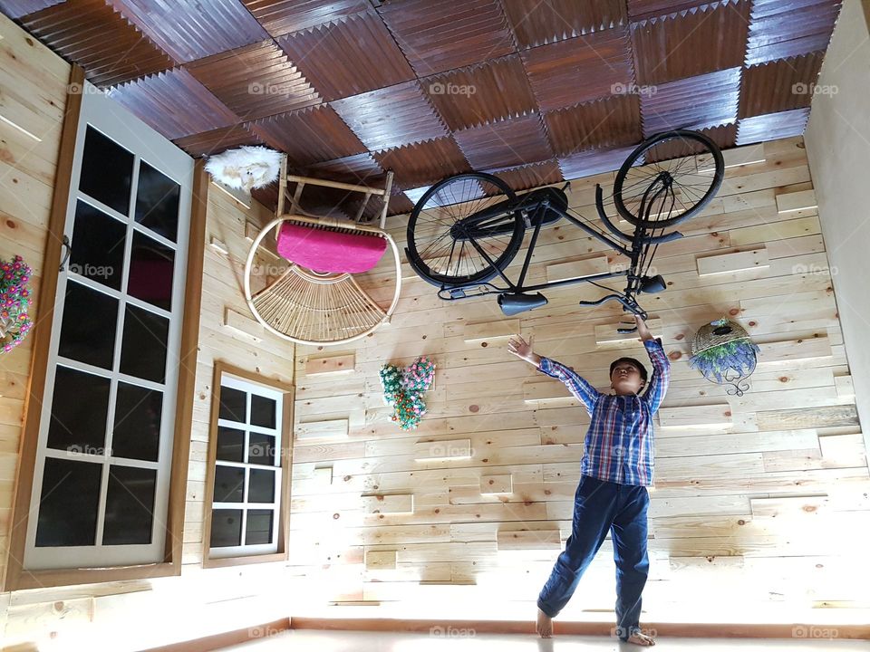 hanging bicycle on the porsh, front porch chairs, brown wooden floors, classic windows, back and forth brick patio walls, decorative flower on the patio wall
