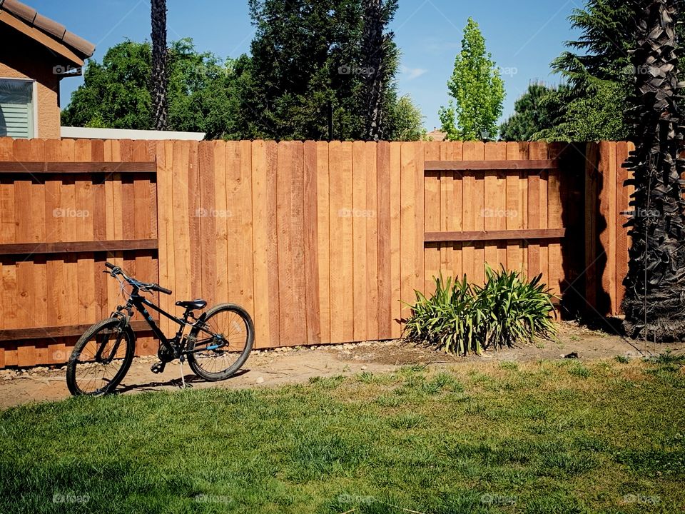 Bike by the wooden cedar fence in the yard on a summers day 