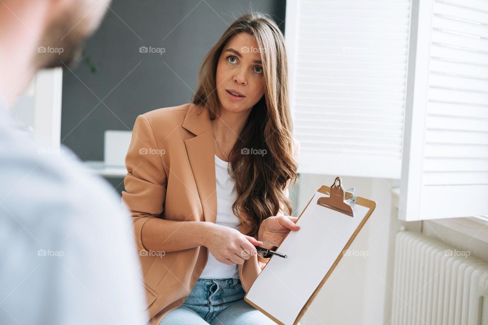 Young brunette woman with long hair in stylish suit working with young man, woman interviews a man in the bright modern office