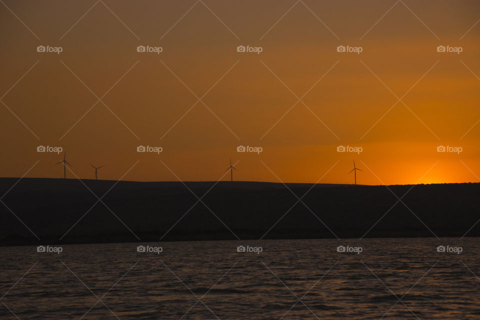 Sunset and wind turbines at river, Natural energy
