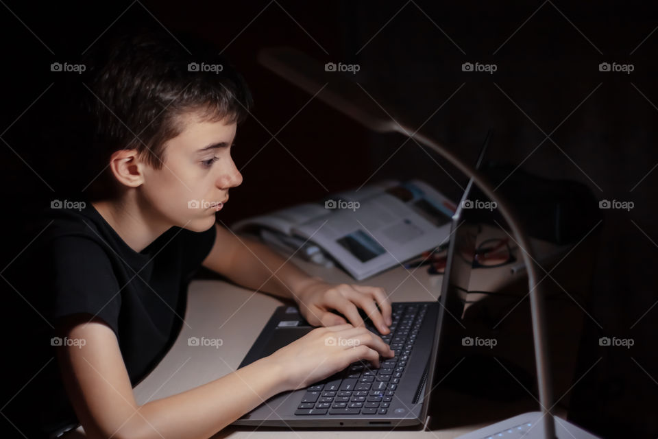Portrait of teenage boy working at laptop with serious expression.