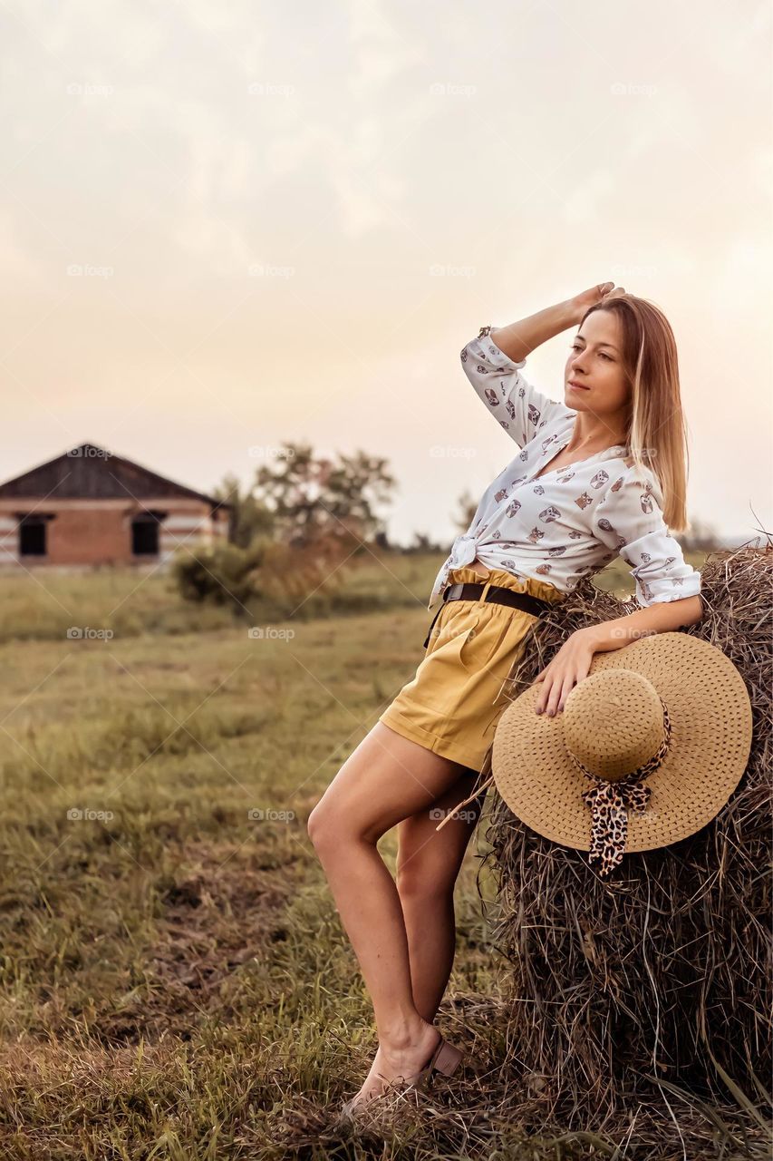 Young blonde girl in a field with haystacks. Favorite summer clothes shorts and shirt