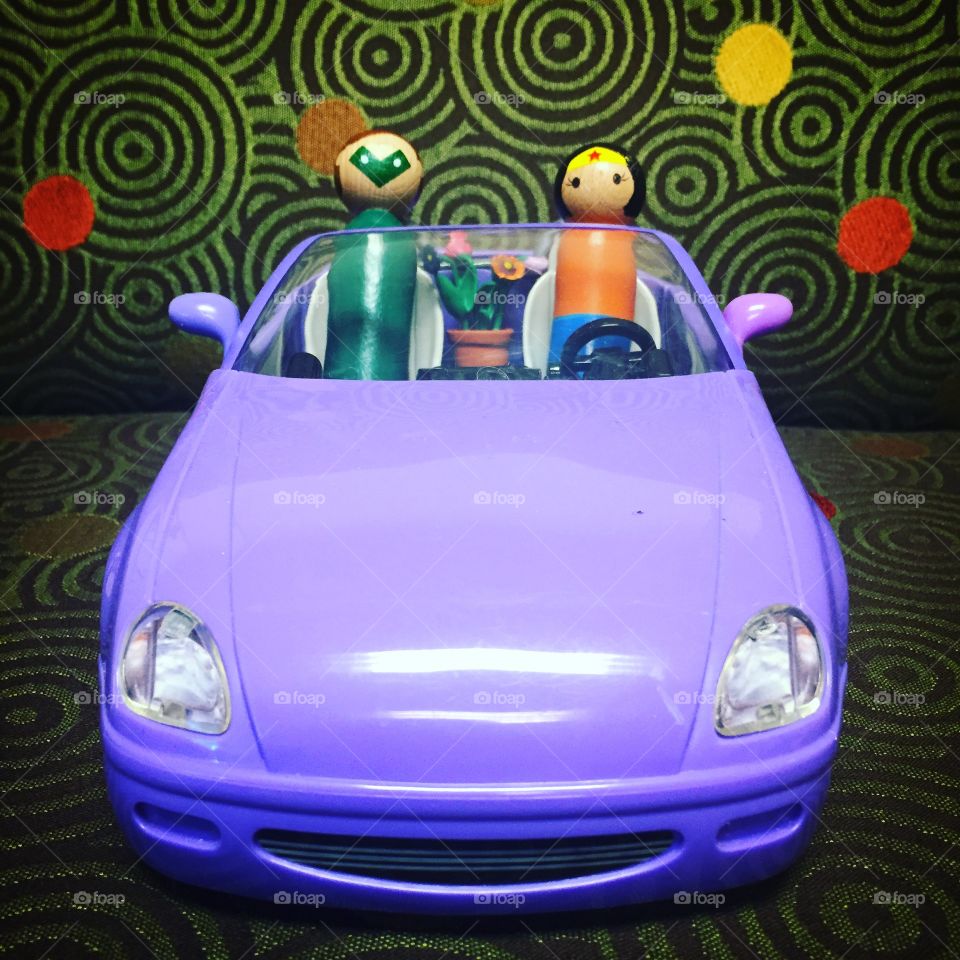 Toy super heroes in a toy car in front of colorful green spiral designs