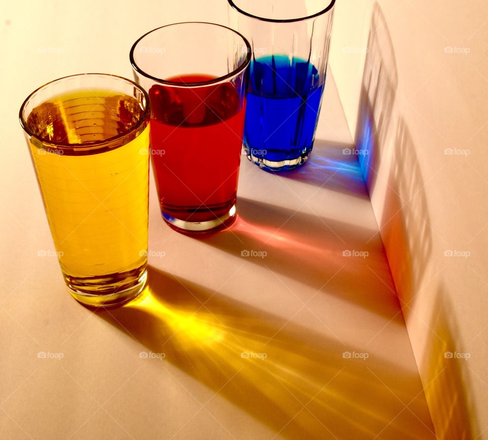 Primary colors fill glasses with colored water and shadows the same color as each glass reflects onto the surface