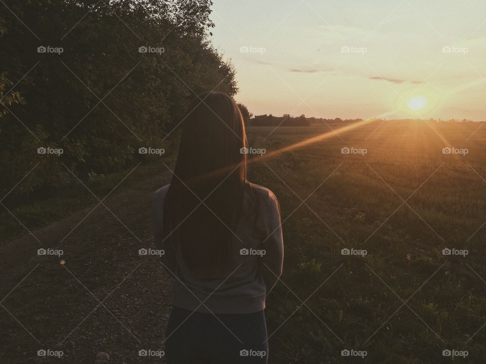 the girl looks at the sunset on a summer evening in the field