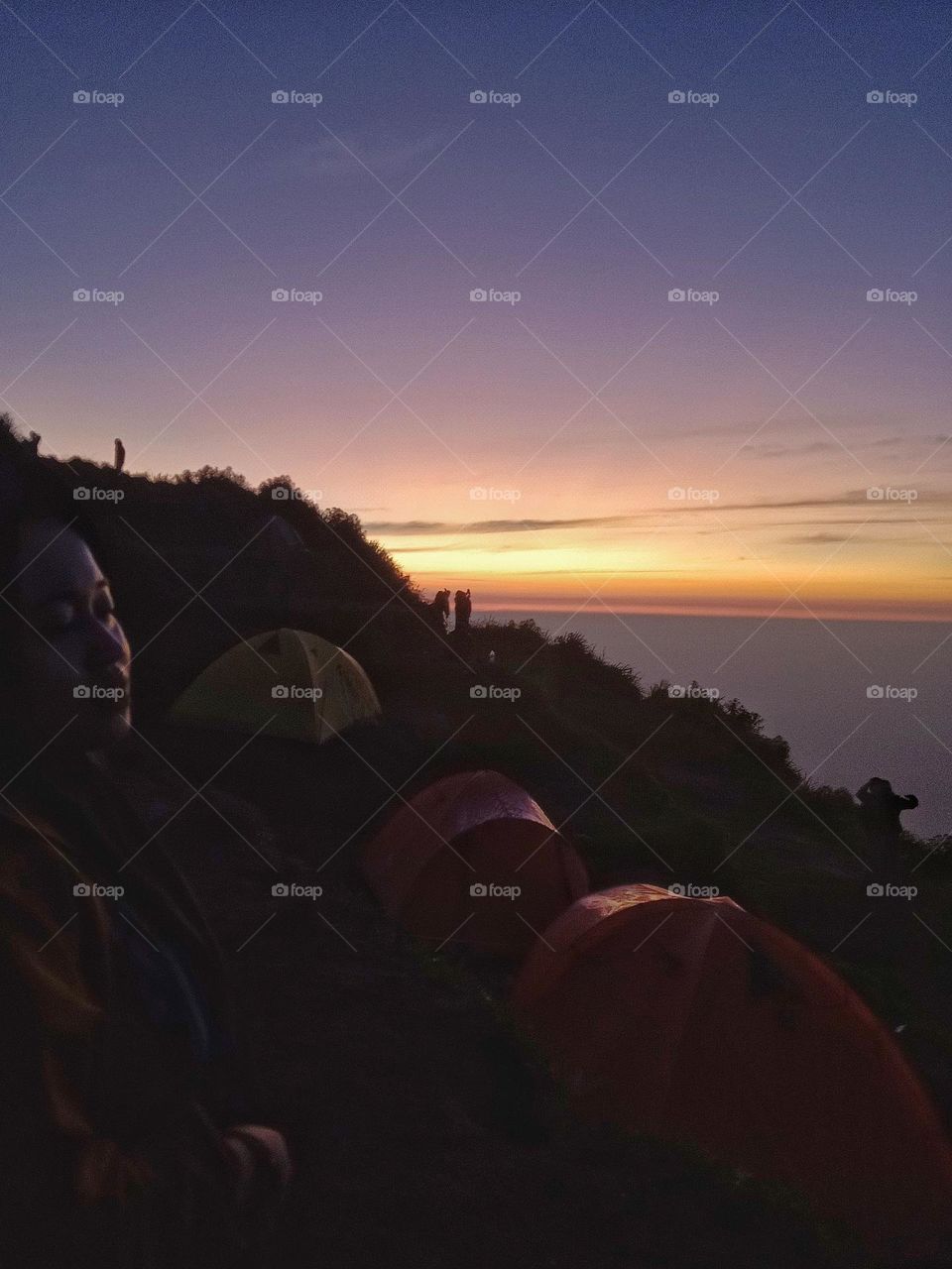 A woman is waiting for the sunrise on the top of a mountain.