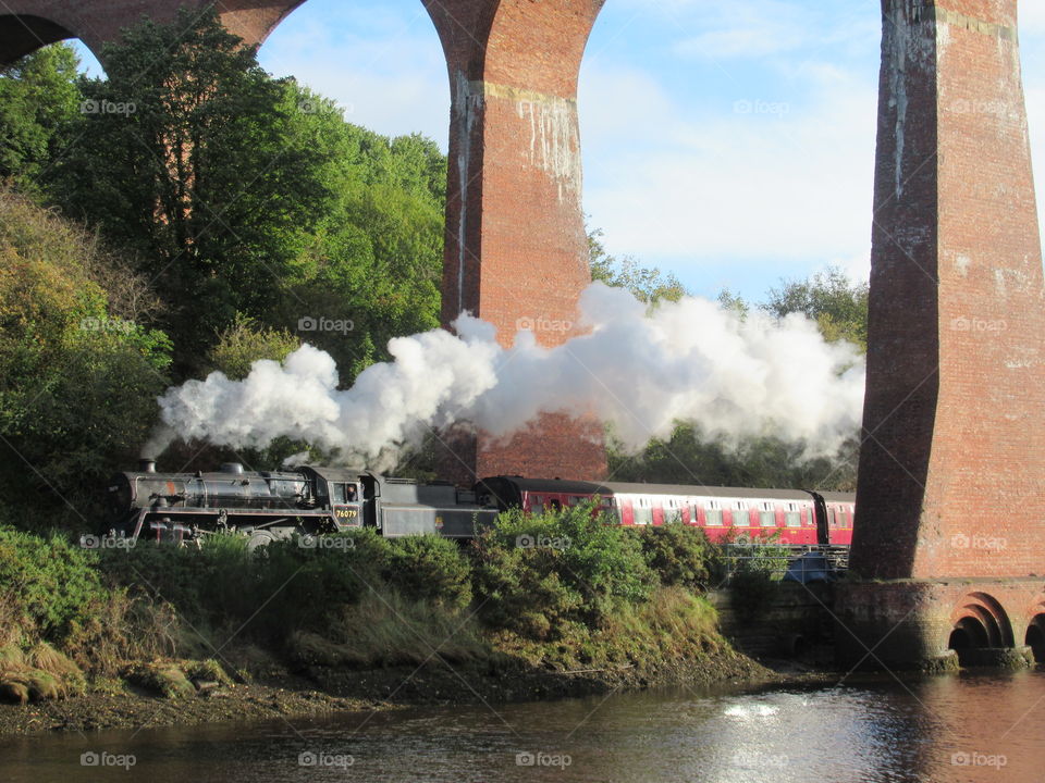 Steam train Going under whitby viaduct with river esk next to railway line