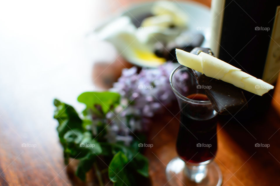 Pieces of white and antioxidant rich dark chocolate with port wine on wood table with lilac flowers  and wine bottle in background epicure vintner vintage conceptual photography 