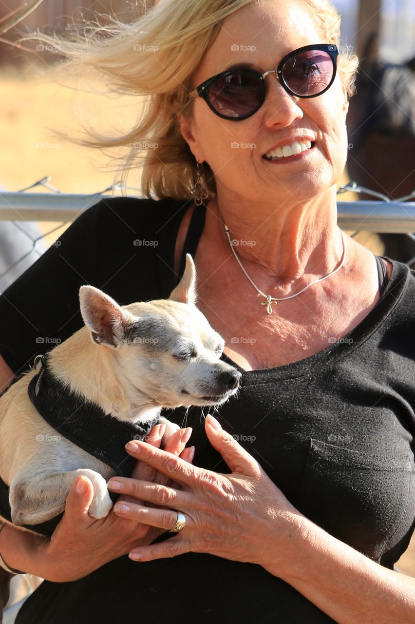 Sixty year old attractive and young looking blonde woman holding chihuahua dog outdoors