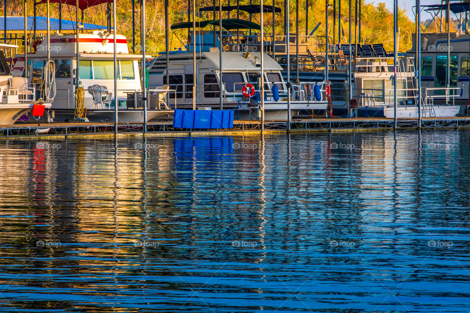 A row of colorful house boats docked in a marina at sunrise with abstract colored reflections in the rippled surface of the water