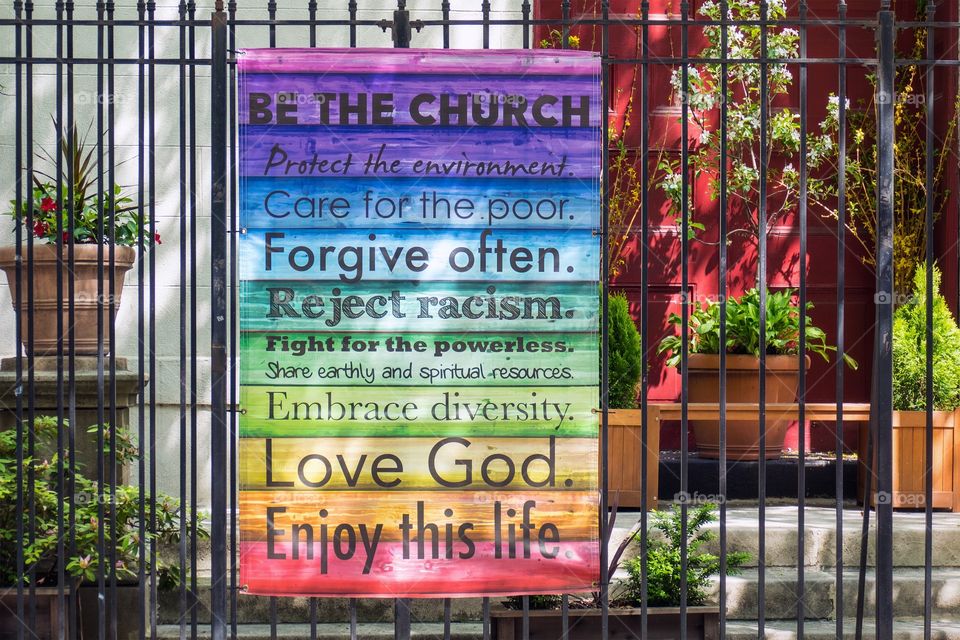 Positive messages written on wood in a variety of colors hanging on a steelfence outside a garden